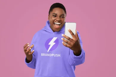 A smiling woman in a BrandPush hoodie checking her phone