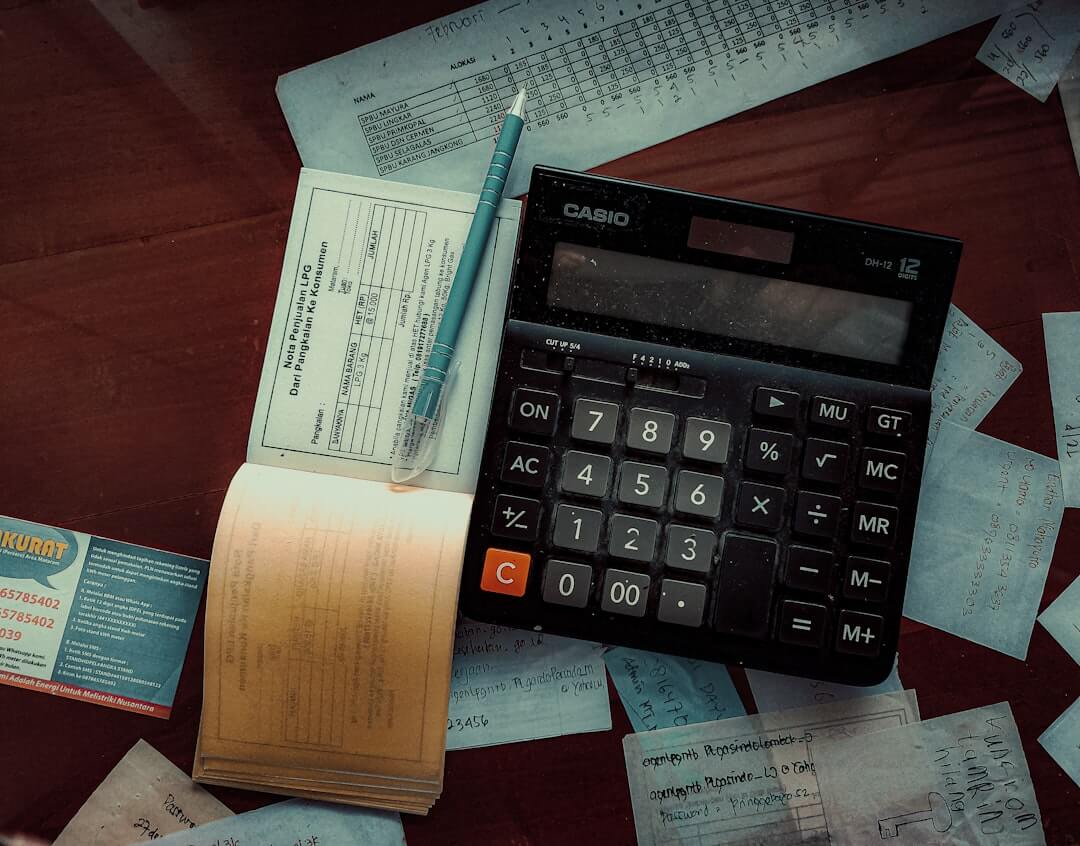 A teal calculator and white pen on a white surface.