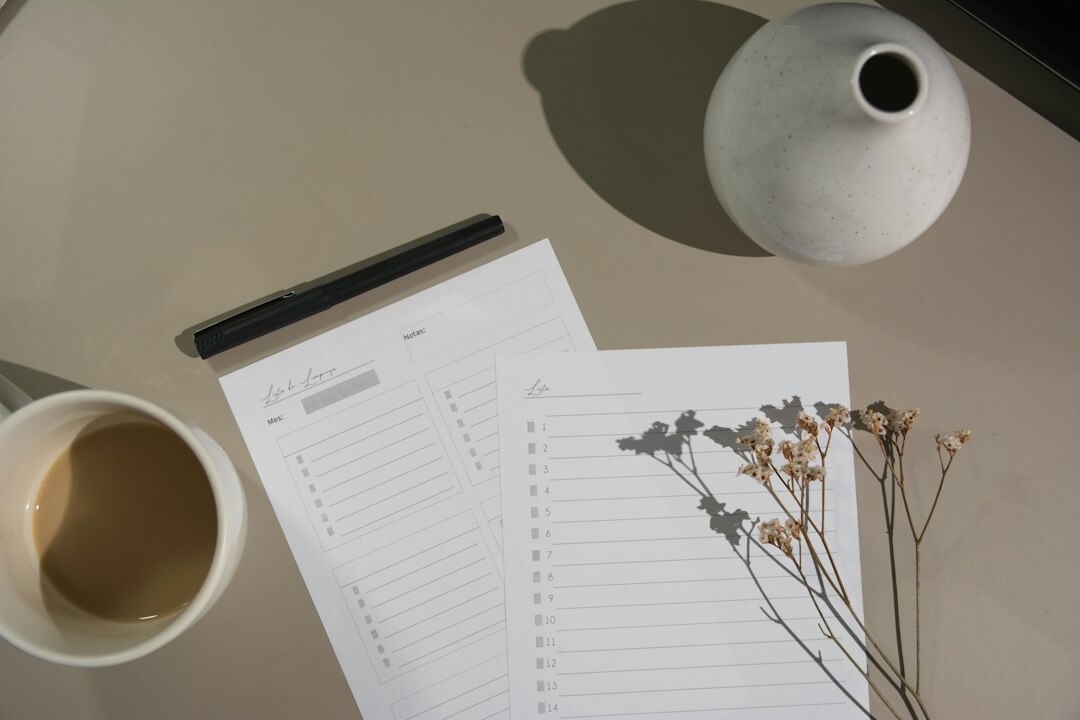 Person writing on clipboard at desk with laptop